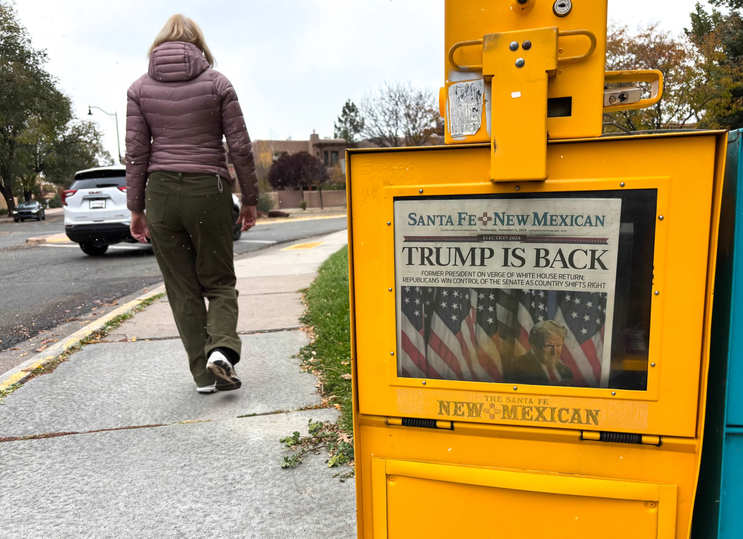 Tech JannHuizenga, Santa Fe, NM: A woman walks past a Santa Fe New Mexican vending box in downtown Santa Fe, where the headline reads “Trump is Back.”